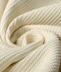 A close up image of an undyed greige waffle knit fabric roll